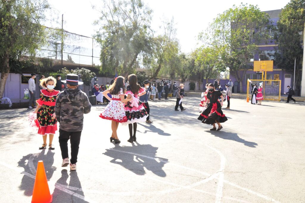 Parejas de estudiantes con trajes típicos bailando cueca frente a sus compañeros